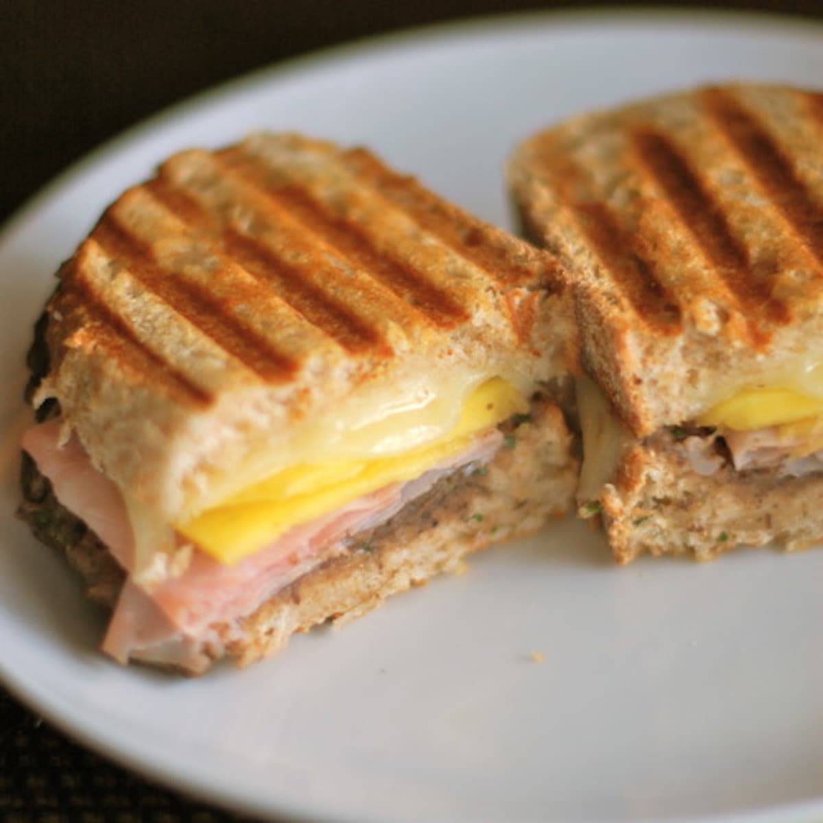 One nuevo cubano sandwich sliced in half on a white plate.