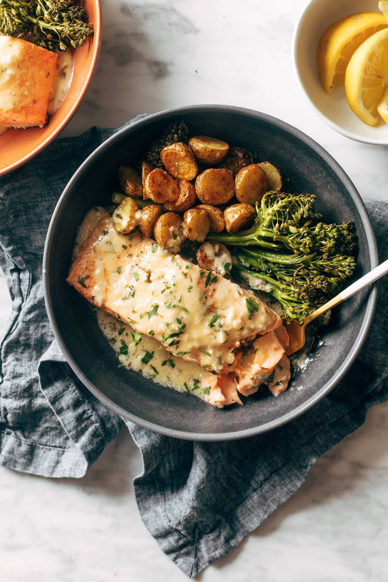 Salmon in a bowl with potatoes, broccoli, and lemon sauce on top.